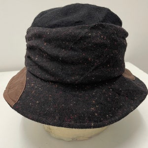 May include: A black and brown tweed bucket hat with a leather trim. The hat has a wide brim and a soft, comfortable feel.