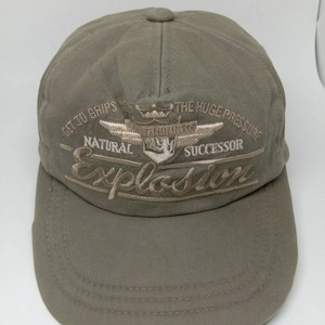 May include: A green baseball cap with a brown embroidered logo that says "Get to Grips with the Huge Pressure - Natural Successor - Explosum".