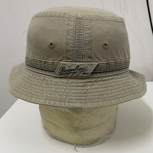 May include: A beige bucket hat with a black and white striped band and the text "Borsalino" in black lettering.