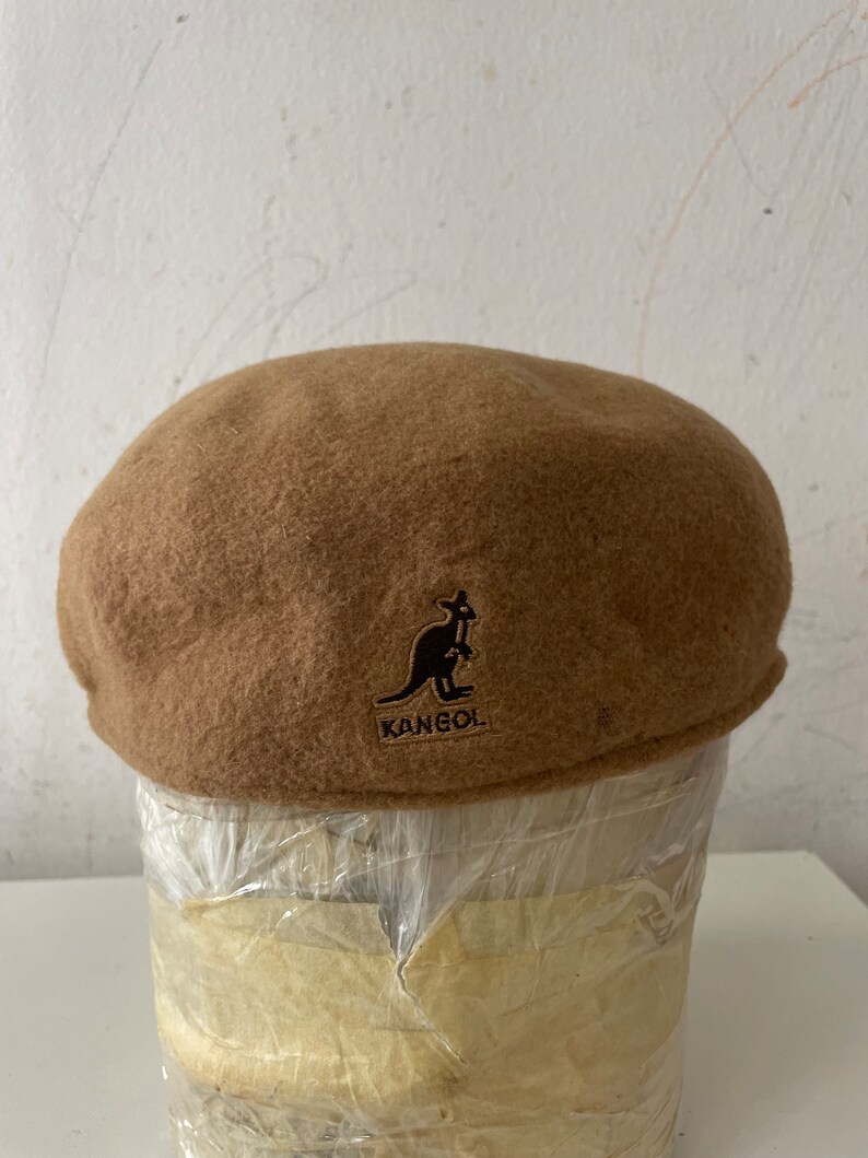 以下が含まれることがあります： カンゴールの茶色のウールベレー帽。茶色のカンガルーのロゴ入り