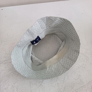 May include: A light gray bucket hat with a textured, woven pattern. The interior features a white sweatband and a dark blue Kangol brand label with a kangaroo logo and the text "KANGOL" and "BLUE" printed in white on the inner rim.
