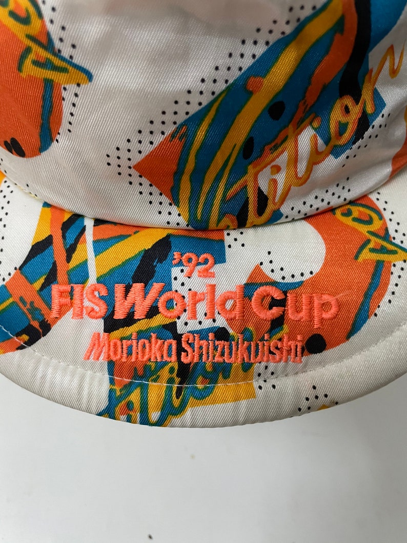 May include: White baseball cap with a colorful geometric pattern and the text "FIS World Cup Morioka Shizukuishi 1992" embroidered in orange.