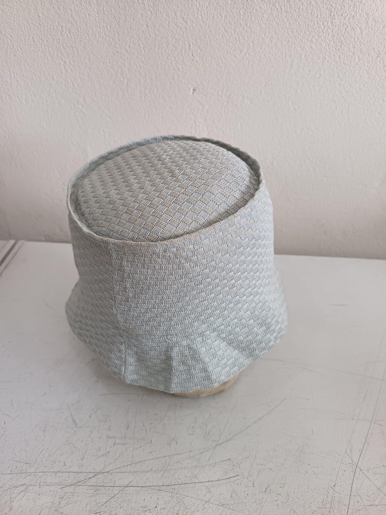 May include: A light gray bucket hat featuring a textured, woven basket-weave pattern throughout the crown and the brim. The hat has a structured, rounded top and a slightly flared, flexible brim, showcasing a consistent light gray color tone.