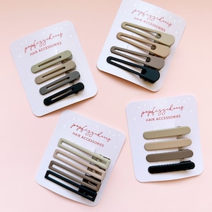 May include: Four sets of hair clips on white cards with the text "popfizzhaus HAIR ACCESSORIES". Each set contains four clips in different shades of brown and black.