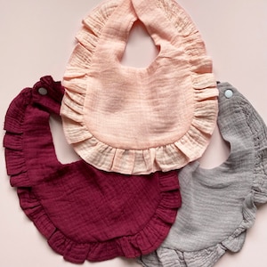 May include: Three baby bibs with ruffled edges. The bibs are in pink, burgundy, and gray.