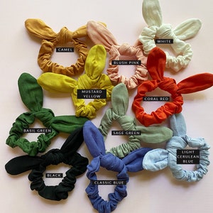 May include: Assortment of 10 colorful hair scrunchies with bunny ear bows. Colors include basil green, camel, blush pink, white, mustard yellow, coral red, sage green, black, classic blue, and light cerulean blue.
