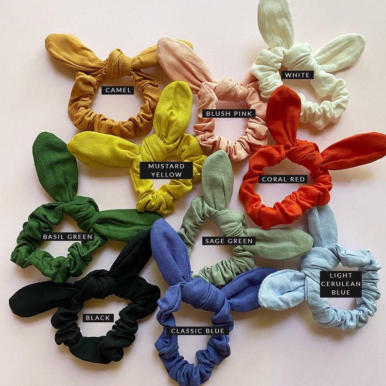 May include: Assortment of 10 colorful hair scrunchies with bunny ear bows. Colors include basil green, camel, blush pink, white, mustard yellow, coral red, sage green, black, classic blue, and light cerulean blue.