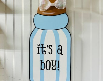 May include: A blue and white striped baby bottle with a brown top and a white bow. The bottle has the text "it's a boy!" written on it.