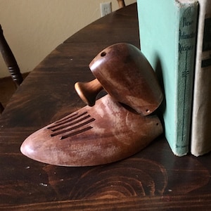 May include: A pair of wooden shoe bookends shaped like a shoe with a carved design. The bookends are holding up two books with green and white covers. The books have the text "New Orleans Recipes" and "The Story of the Old South" on the spines.