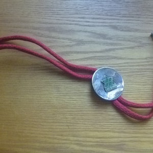 May include: A red bolo tie with a silver round pendant featuring a green star with the text "1961-1963" inside.