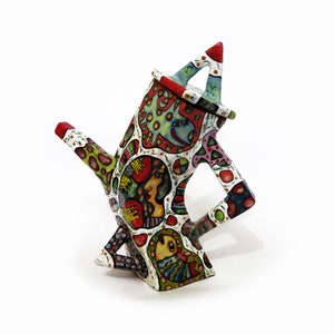 May include: A colorful ceramic teapot with a whimsical design. The teapot is decorated with a variety of shapes, patterns, and colors, including red, green, blue, and yellow. The teapot has a unique, angular shape and a spout that curves upwards.