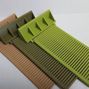 May include: Three plastic trays with a grid pattern and a raised section at one end. The trays are in shades of green and tan.