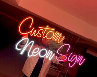 May include: A neon sign with the words "Custom Neon Sign" in orange, white, and pink. The sign is illuminated and held up by a person. The background is a warm, reddish-orange color.