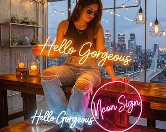 May include: A neon sign featuring the text Hello Gorgeous in a cursive script. The sign emits a warm yellow glow and is mounted on a clear acrylic backing. The text is displayed in a single line, creating a bright and illuminated decorative piece.