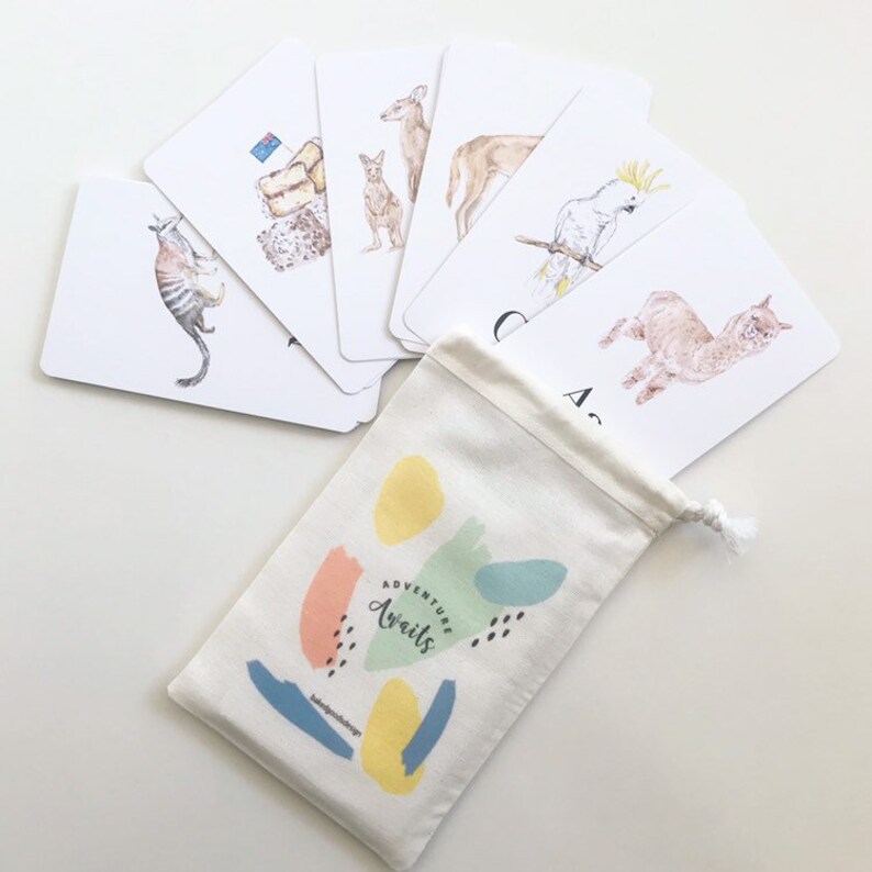 Puede incluir: Un juego de flashcards con animales australianos, incluyendo un canguro, un kookaburra, un wombat y un equidna. Las tarjetas son blancas con ilustraciones coloridas y se empaquetan en una bolsa de cord&oacute;n blanco con el texto "Adventure Awaits".