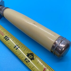 May include: A vintage-style bottle opener with a cream-colored handle and silver-toned metal accents. The handle is approximately 4 inches long. A yellow measuring tape is in the foreground, showing measurements in inches.