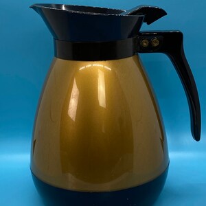 May include: A gold-colored thermal carafe with a black lid and handle. The carafe has a black base.