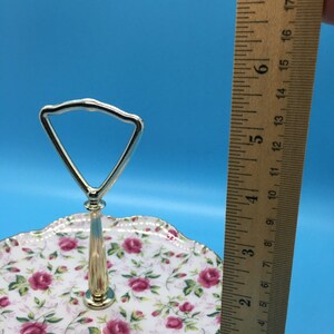 以下が含まれることがあります： バラの花柄の2段サービングトレイ。トレイには金色のハンドルとトリムが付いています。トレイの直径は約18cmです。