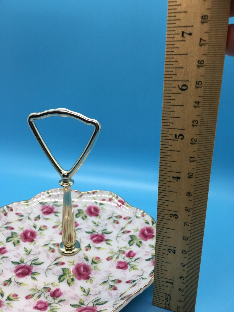 以下が含まれることがあります： バラの花柄の2段サービングトレイ。トレイには金色のハンドルとトリムが付いています。トレイの直径は約18cmです。