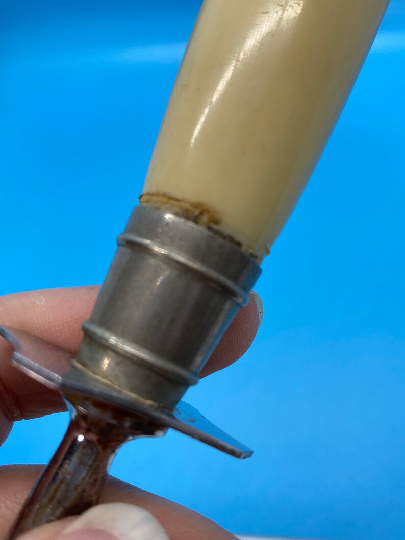 May include: Close-up of a vintage knife with a cream-colored handle and a silver metal bolster. The handle appears to be made of a smooth, glossy material. The blade is visible, with a silver metal finish.