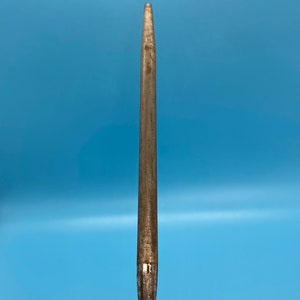 May include: A metal knife sharpener with a long, tapered steel rod. The rod is a dull silver color with signs of wear. The base of the sharpener has a decorative, star-shaped design. The background is a solid light blue.