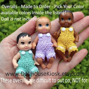 May include: Three crocheted doll overalls in different colors: lavender, yellow, and green. The overalls have white buttons and are made to order. The text "www.DollhouseKiosk.etsy.com" and "14+ These overalls are difficult to put on, NOT for kids!" is visible in the image.