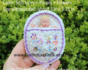 May include: A soft ivory and purple crochet snuggle wrap pocket with flower embellishments, holding a small doll. The pocket measures approximately 3 inches by 3.75 inches. The text on the image reads "Crochet Snuggle Wrap Pocket as Shown" and "NOT for small kids please!"