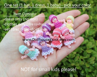 May include: A collection of miniature crocheted baby dolls in various colours, including pink, purple, yellow, and green. Each doll is wearing a crocheted dress and hat. The dolls are displayed on a hand, with the text "www.DollhouseKiosk.etsy.com" and "NOT for small kids please!" visible below.