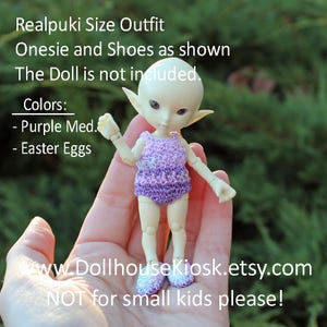 May include: A Realpuki size outfit, including a purple onesie and matching shoes, is shown. The doll is not included. The outfit is available in Purple Med. and Easter Eggs colors. The website is www.DollhouseKiosk.etsy.com. Not for small kids.