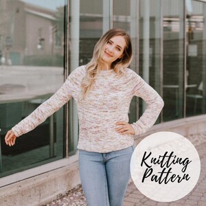 May include: A woman wearing a white, pink, and yellow speckled sweater with a round neckline and long sleeves. She is standing in front of a glass building. The text "Knitting Pattern" is written in a circle in the lower right corner of the image.