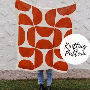 Peut inclure: Une couverture en tricot blanche avec un motif géométrique de demi-cercles orange. La couverture est tenue devant un mur blanc avec le texte "Knitting Pattern" dans un cercle blanc.