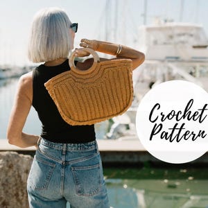 May include: A crocheted tote bag with a wooden handle. The bag is a light brown color and has a slightly curved shape. The bag is being held by a person wearing a black tank top and blue jeans.