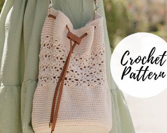 Puede incluir: Un bolso de crochet blanco con forma de cubo, con una correa de cuero marrón y un cordón de ajuste. El bolso lo lleva una persona que lleva un vestido verde. El texto "Crochet Pattern" es visible en la imagen.