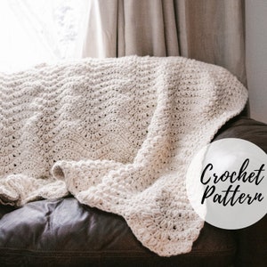 Puede incluir: Una manta de crochet blanca con un patrón de puntadas texturizadas, drapeada sobre un sofá de cuero marrón. El texto "Crochet Pattern" está escrito en negro sobre un círculo blanco.