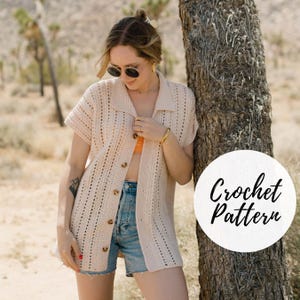 May include: A woman wearing a crocheted cardigan with a collared neckline and short sleeves. The cardigan is a light beige color and has a button closure. The woman is wearing blue denim shorts and has her hair pulled back in a ponytail. The image has the text "Crochet Pattern" in a white circle.