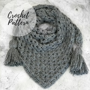 May include: A gray crochet shawl with a triangular shape and two tassels. The shawl features a textured stitch pattern and the words "Crochet Pattern" in a handwritten font.