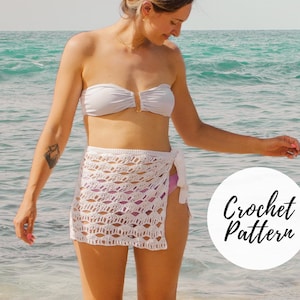 May include: White crochet wrap skirt with a tie detail. The skirt is shown on a model standing on a beach. The text "Crochet Pattern" is in a circle on the right side of the image.