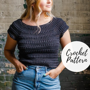 Puede incluir: Un top de ganchillo gris oscuro con un patrón texturizado y mangas cortas. El top se combina con vaqueros azules. La imagen incluye un círculo blanco con las palabras "Crochet Pattern" en letra cursiva.