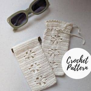 May include: Crochet pattern for a white crocheted sunglasses case with a floral design. The case has a drawstring closure and is shown with a pair of green sunglasses.
