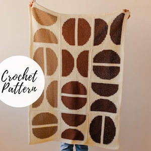 May include: Crochet pattern for a geometric blanket with brown and beige circles on a white background. The blanket is being held up by a person.
