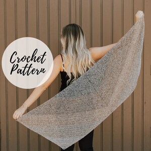 Può includere: Una scialle all'uncinetto grigio argento è esposto, tenuto aperto per mostrare la sua forma triangolare. Le parole "Crochet Pattern" sono in un cerchio bianco in alto a sinistra. Lo scialle è tenuto da una persona che indossa un top nero e pantaloni neri.
