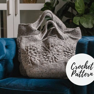 Puede incluir: Una bolsa de mano de crochet gris con un patrón texturizado. La bolsa está sentada en un sofá azul con un círculo blanco que dice "Crochet Pattern".