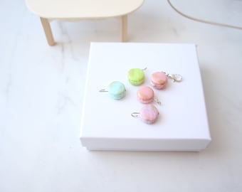May include: Five pastel-colored macaron charms with silver jump rings. The macarons are light green, pink, and white with gold accents.
