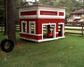 May include: A red wooden playhouse with a white trim and the words "Firehouse P.A." on the front. The playhouse has a garage door and a window. There is a red toy car inside the garage.