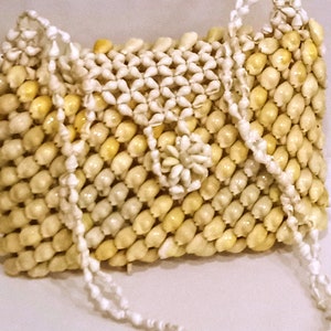 Puede incluir: Un bolso de mano blanco y crema hecho de conchas tejidas. El bolso tiene una correa larga hecha de cuentas blancas.