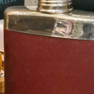 Può includere: Una fiaschetta d'argento e bordeaux con tappo a vite.