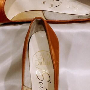 May include: A pair of brown leather high-heeled shoes with gold lettering on the inside. The lettering reads "*Source" and "P. Dolcis".
