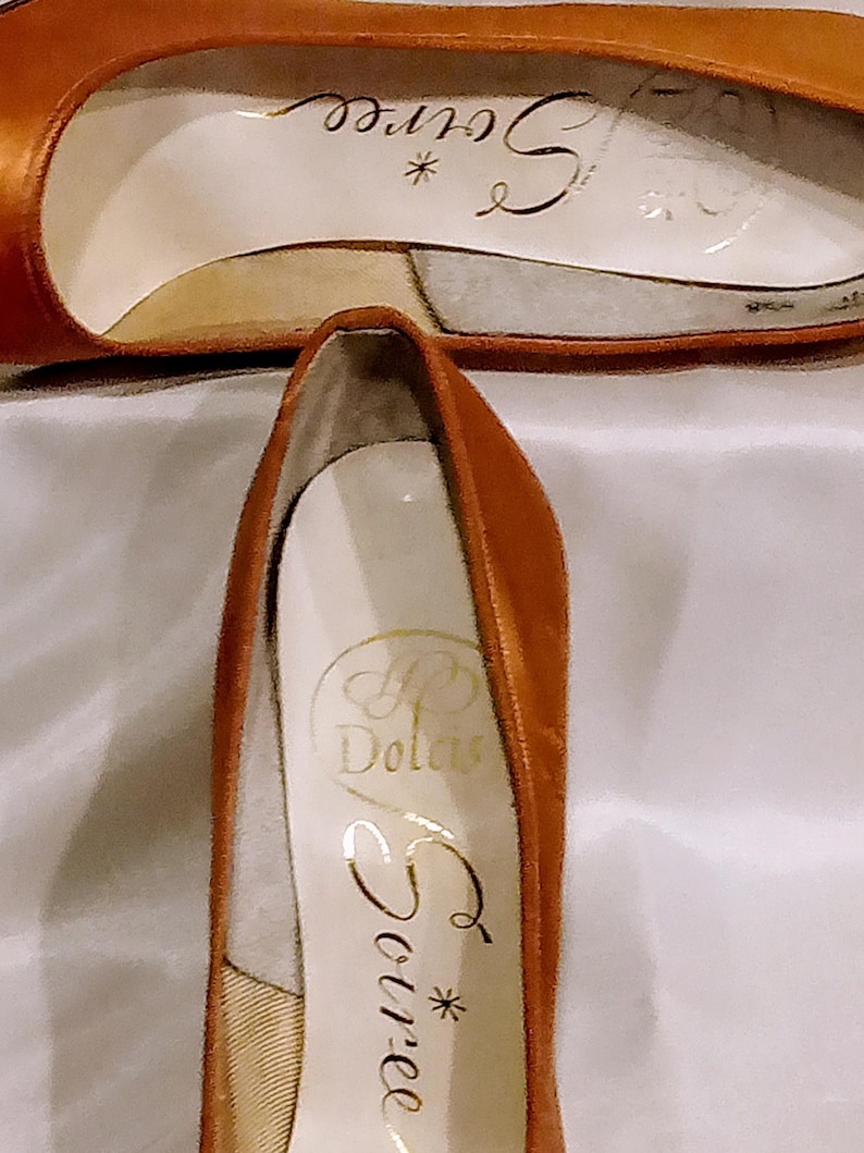 May include: A pair of brown leather high-heeled shoes with gold lettering on the inside. The lettering reads "*Source" and "P. Dolcis".