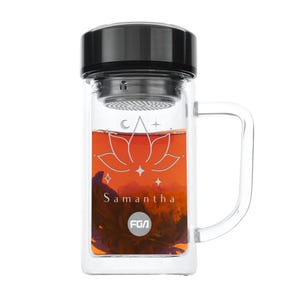 May include: A clear glass tea infuser bottle with a black lid and a handle. The bottle contains loose leaf tea and has a white lotus flower design with the name "Samantha" and the text "FGA" printed on it.