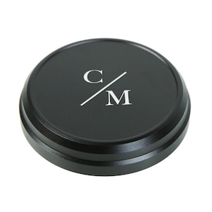 May include: Black round camera lens cap with a silver C/M logo.